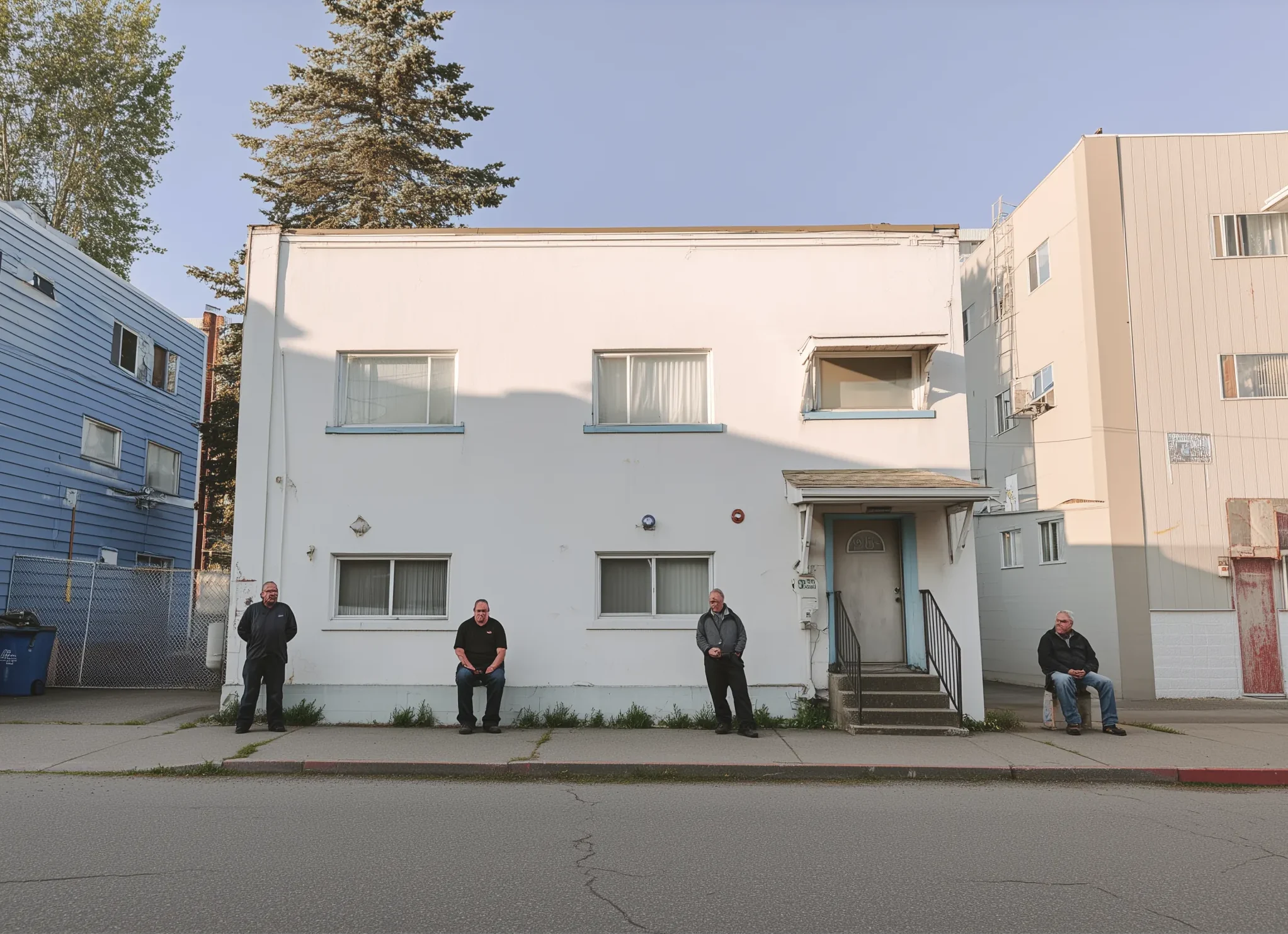 Residents standing and sitting outside a transitional housing building in Northern BC, illustrating supportive housing, community presence, and stability-focused services.